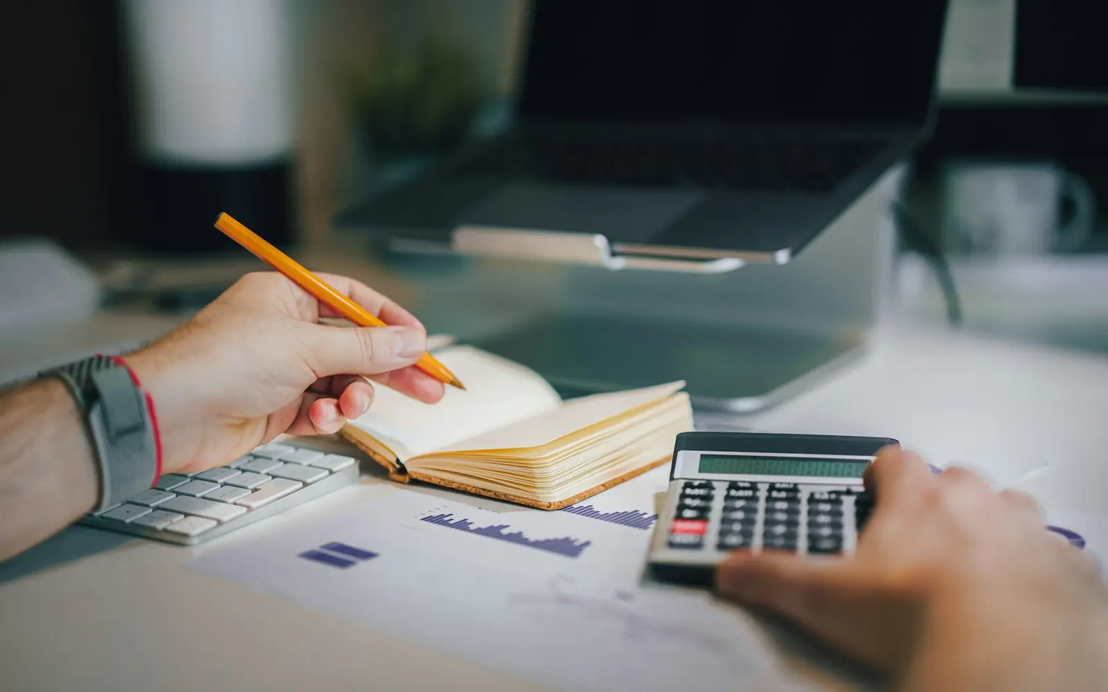 A person working out a budget with a calculator, a notebook and a laptop