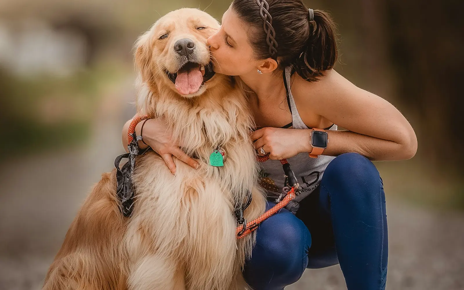 A woman kissing a happy golden retriever on the cheek
