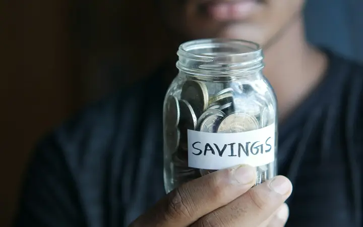 A person holding a glass jar of coins labeled savings