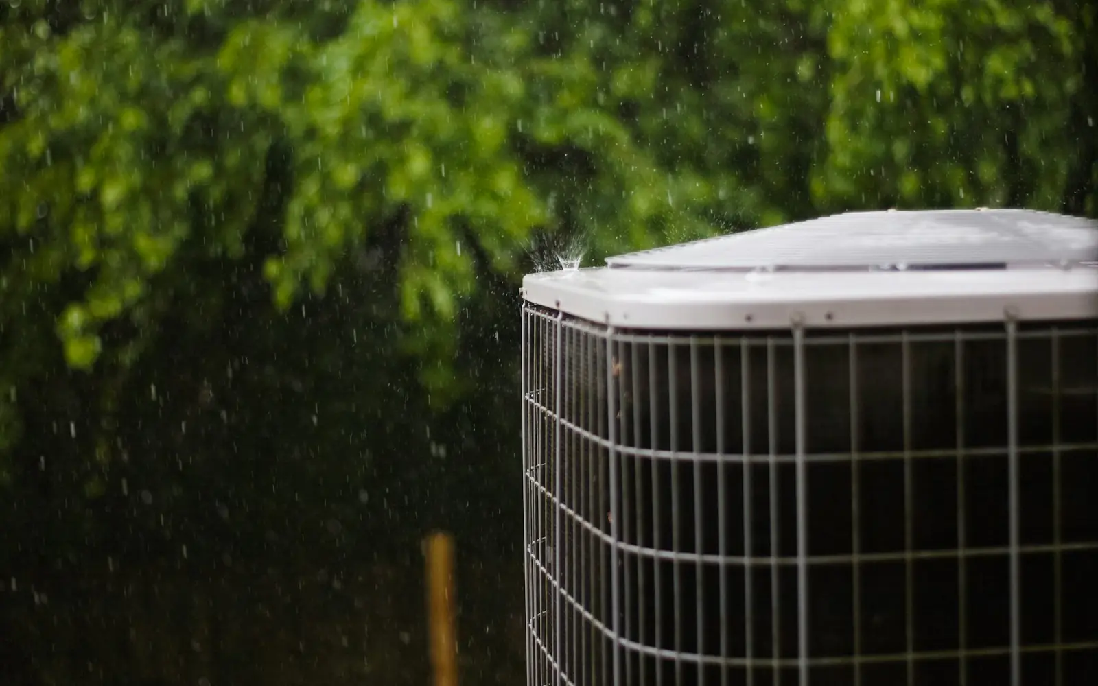 Central air conditioner unit outside a house, next to green shrubs